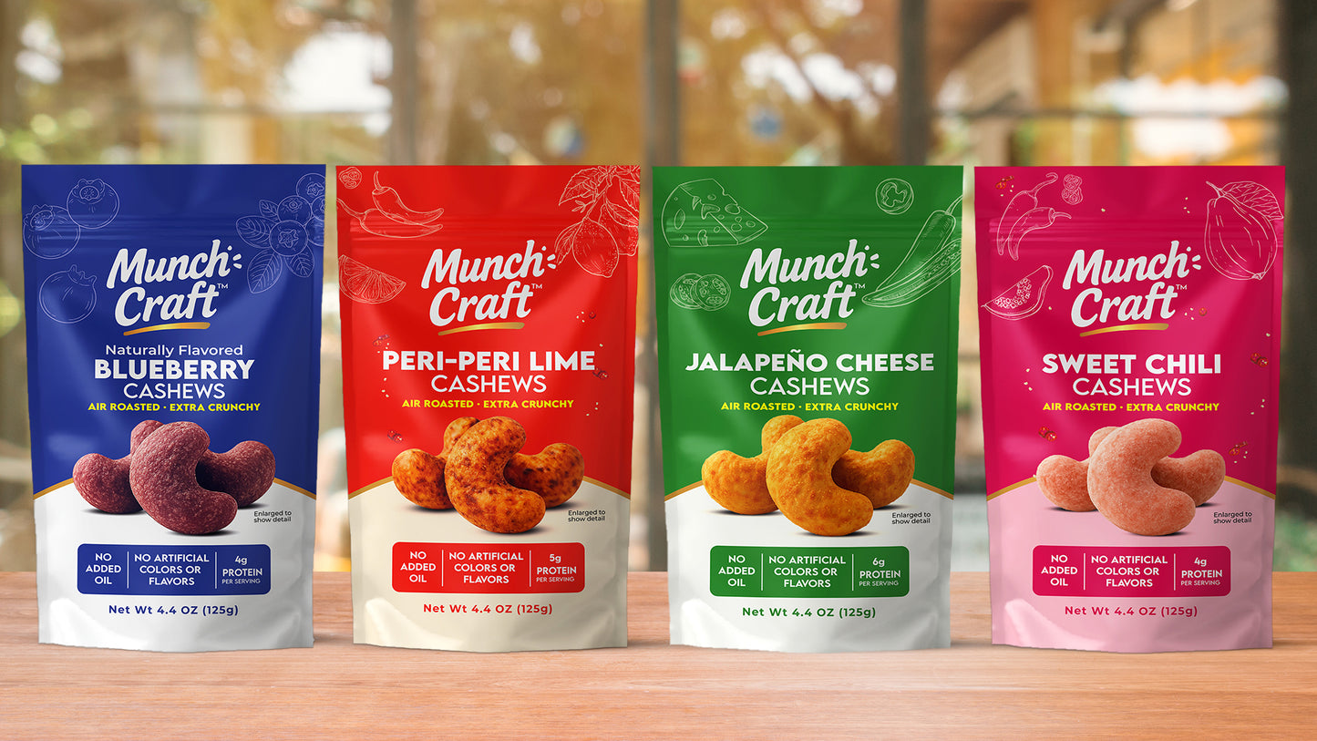 Four Munch Craft cashew snack packages on a wooden surface with a blurred background.